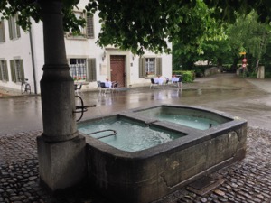 Fountain framed by restaurant tables in the rain