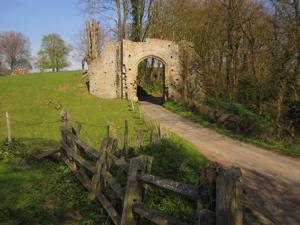 Ruined stone gate (New Gate at Winchelsea) over road, surrounded by fields and trees