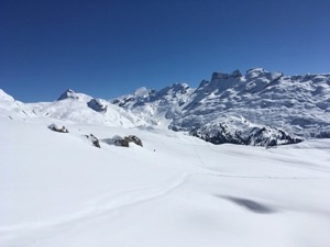 Snow covered mountains framing snow covered fields under blue sky