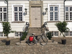 Bicycle with red panniers leaning against the steps to a house.