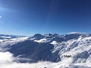 Blue skies, over snow covered mountains with clouds nestling in the valleys