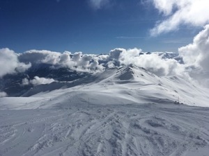 Snow covered piste, with mountains in the background.