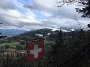 View across hills with light snow cover, Swiss flag in foreground.