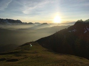 View along the alps, with the sun setting and clouds creeping through the valleys