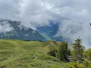 View down a narrow path down along an arête, Glarus valley in the background & clouds rolling in.