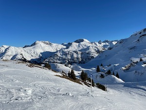 Snow covered ski pistes framed by mountains under blue skies.