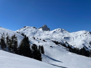 Snow covered mountains with tracks of ski pistes under blue skies.