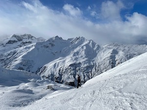 Ski-piste in front of snow covered mountains under blue skies.