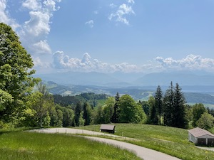 View over green hills down to the Zurisee, mountains in the background. Scattered clouds but bright and sunny.