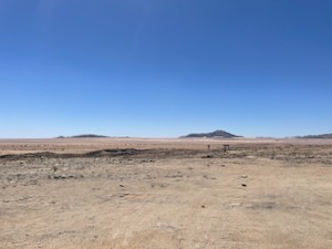 View over barren dessert, small mountains in the distance.