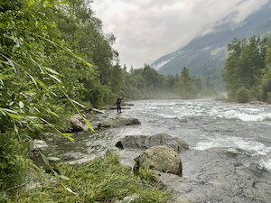 Fishing from a rock beside the river, mist rising from the water.