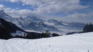 View down the valley from Fluegenspitz, across a snow field and with mountains in the background