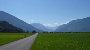 Flat road along valley floor, with green fields on either side and Glarus mountains in the background